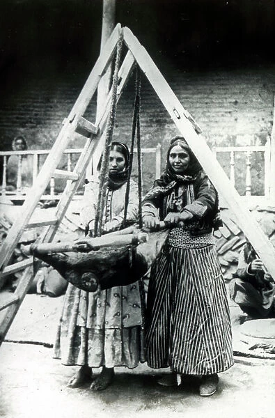 Two Persian women rocking a goatskin to churn milk