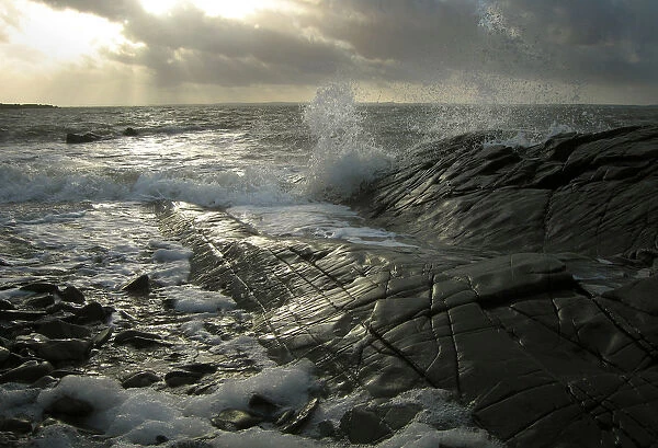 Waves splash against the shining black rocks at Knockbrex