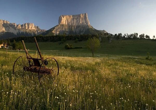 Mont Aiguille at dawn, with hay meadow. Limestone peak in Vercors, east France. Old farm implement in the foreground