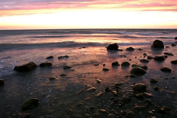 Sunrise at sea beach with boulders and approaching waves Moen Peninsula, Denmark