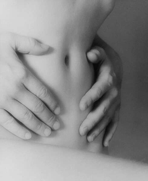 Abdomen. Side view of a womans hands resting on her naked abdomen