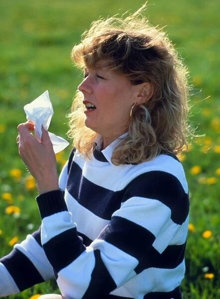 Woman sitting in meadow sneezing