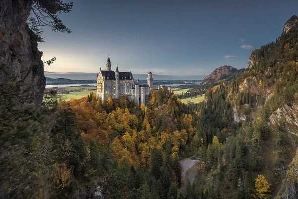 Dusk lights on Neuschwanstein Castle surrounded by colorful woods in autumn, Fussen