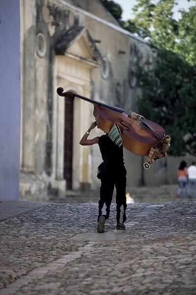Musician carrying double bass along cobbled street to Plaza Mayor, Trinidad