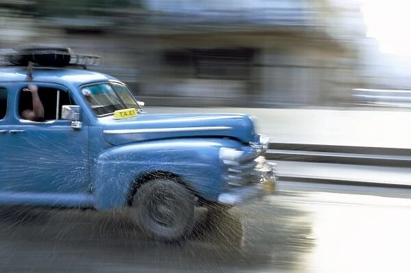 Panned shot of old American car splashing through puddle on Prado, Havana