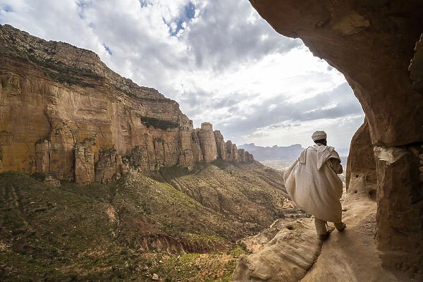 Rear view of priest walking on access trail to the rock-hewn Abuna Yemata Guh church