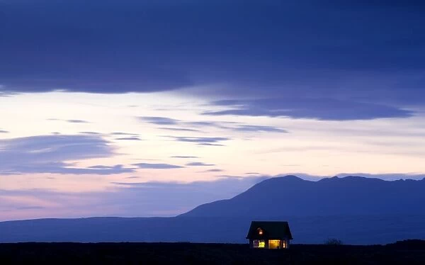 Twilight view towards mountains with small house illuminated by interior lights