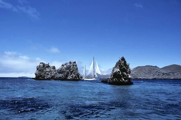 Yacht Aspasia Alpha sailing past Devils Crown, off Punta Cormorant. Floreana Island, Galapagos, Ecuador