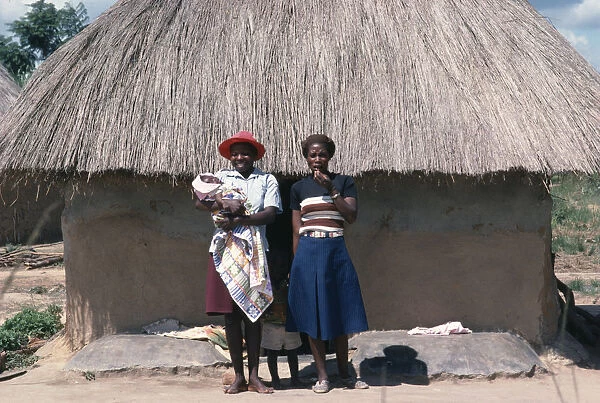 20040259. ZIMBABWE General Young Shona women and children standing outside thatched hut