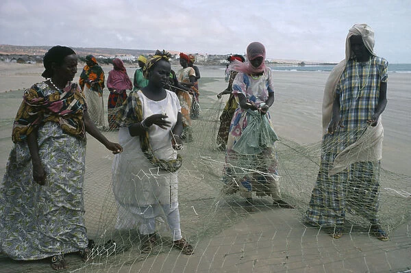 20053340. SOMALIA Industry Settled nomad women mending fishing net on shore of beach