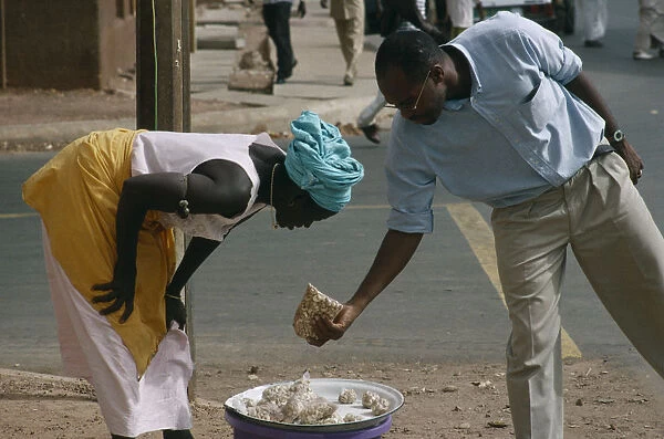 20075209. GAMBIA Markets Woman selling Cashew nuts to a man along the road side