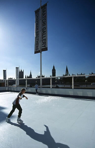England, London, Boy on an Ice skating rink under a sign for th Saatchi Gallery on the bank of the River Thames with the city skyline in silhouette behind