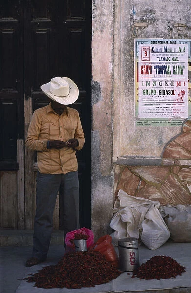 MEXICO, Oaxaca Man standing beside crumbling plaster wall with pile of red chillies
