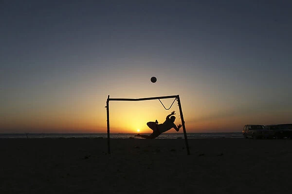 A boy jumps to save a goal while playing soccer on the beach in Benghazi