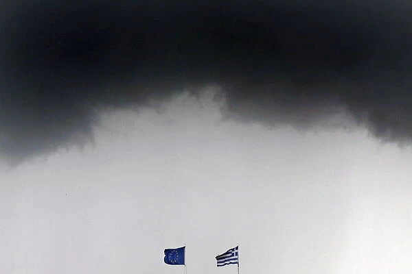 A Greek national flag and an EU flag flutter under storm clouds in Athens