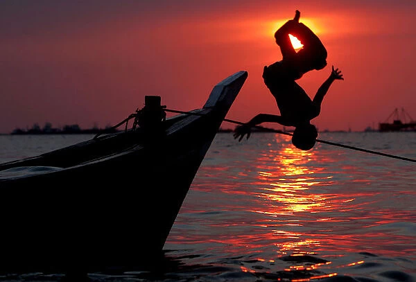 Indonesian boys do somersaults from a wooden boat in Jakartas shore