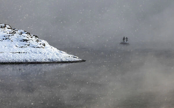 Two local residents row on a boat through a frosty fog as they cross the Shumikha