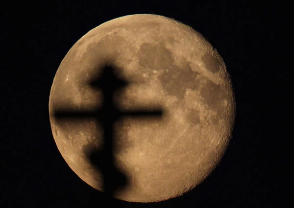 An Orthodox cross is silhouetted against the full moon near the village of Chist, Belarus