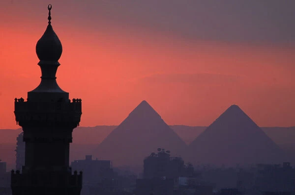 The sun sets on the minarets and the Great Pyramids of Giza in Old Cairo