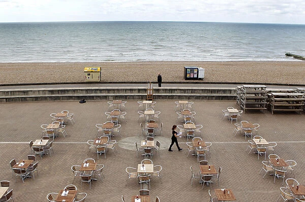 A woman places menus on tables outside a restaurant on the seafront in Brighton
