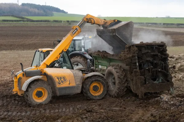 JCB Loadall telehandler loading muck into muck spreader, for spreading on arable field, England, march