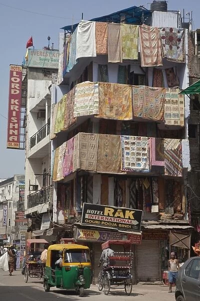 View of city street with rickshaws, hotels and shop selling rugs, Delhi, India