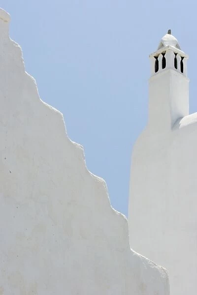 Greece, Mykonos, Hora. Whitechurch belfry against light blue sky and irregular wall