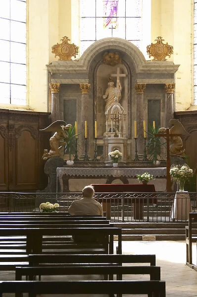 A man contemplating on a bench in a church in front of the altar with a ray of sunshine