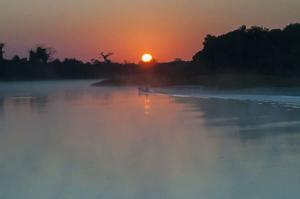 South America, The Pantanal, Brazil, A lone boat at sunrise driving through the rising