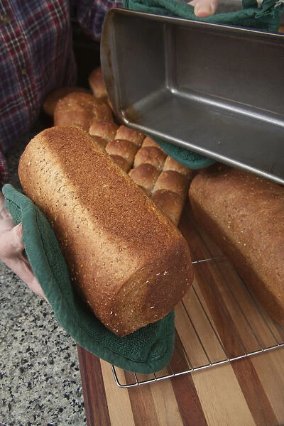 Woman removing loaf of just baked multigrain bread from bread pan. (MR)