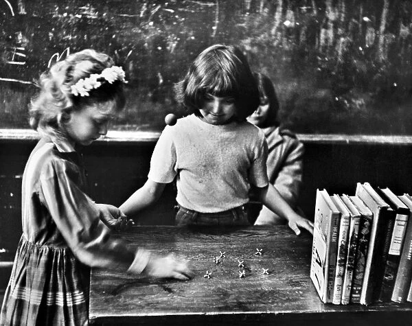 Two 5th grade girls playing jacks on the teachers desk before school in Clairfield, Tennessee. Photograph by Jack Corn, 1964