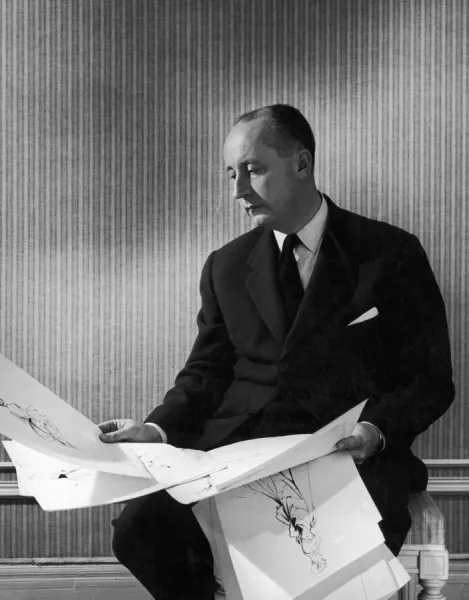 CHRISTIAN DIOR (1905-1957). French fashion designer. Dior looking over some of his sketches for womens dresses, 1940s or 1950s