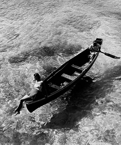 JAMAICA: ROWBOAT, 1946. A fashion model sitting on the edge of a rowboat, with