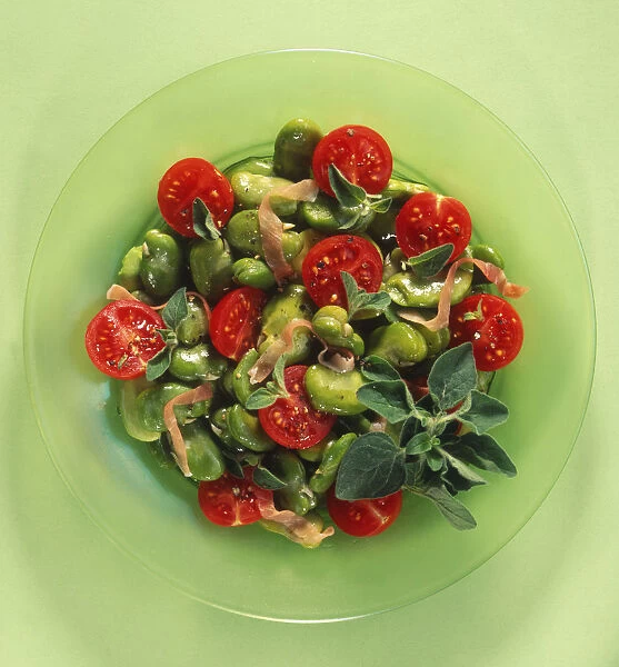 Broad bean and Parma ham salad with red tomatoes on glass plate, close-up