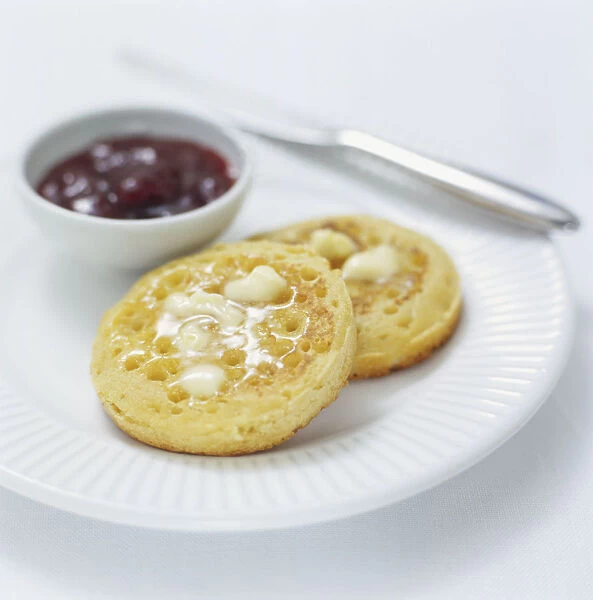 Butter melting on crumpets served on a plate with jam, close up