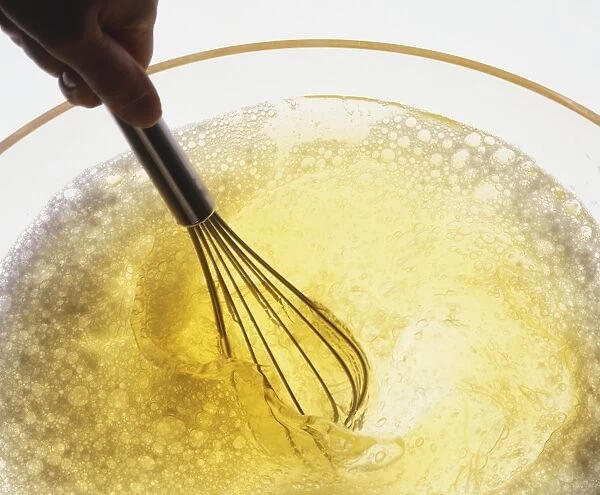 Close-up, whisking an egg white with small metal whisk, egg frothing in clear glass bowl