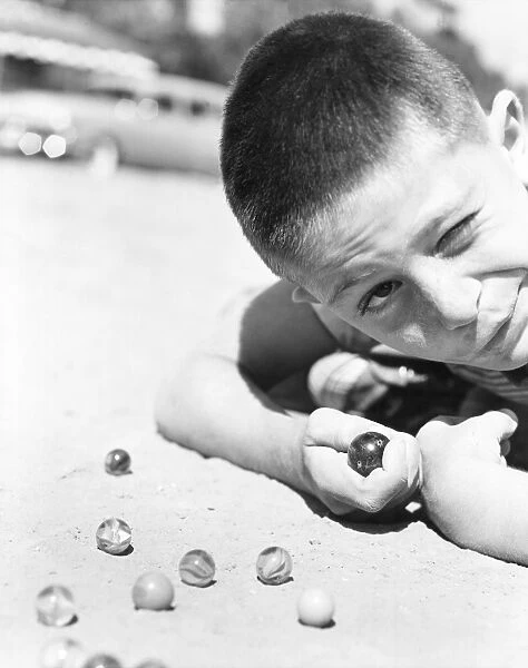 Close-up of young boy playing marbles in the dirt