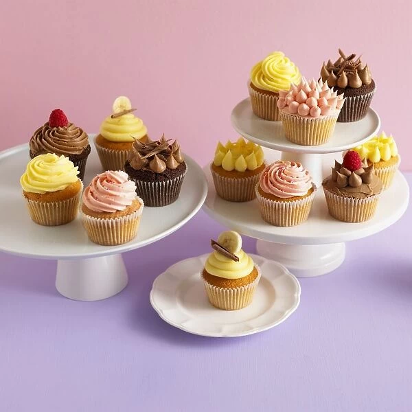 Cupcakes with different flavoured icings, including chocolate, raspberry, lemon and banana, arranged on cake stands and a plate