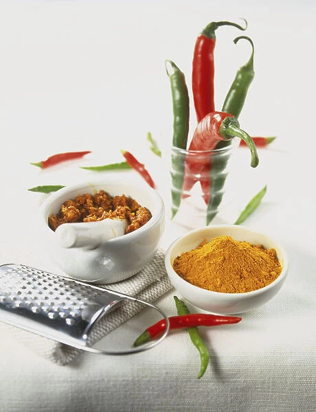 Curcuma longa, ground Turmeric in small ceramic bowl, ground spices in pestle and mortar, metal grater, fresh green and red Chilli Peppers in jar