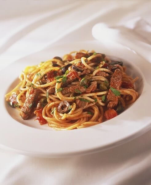 Plate of spaghetti pizzailola with strips of fried red meat, sprinkled with fresh herbs, close up