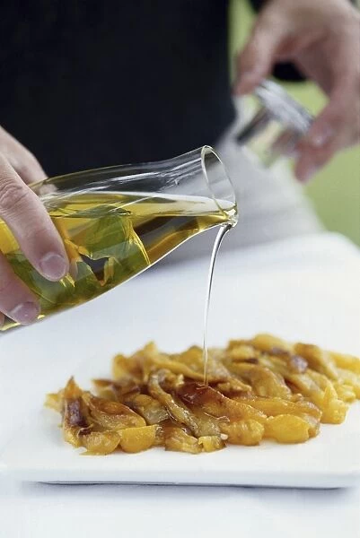 Pouring olive oil from glass serving bottle over roasted yellow peppers