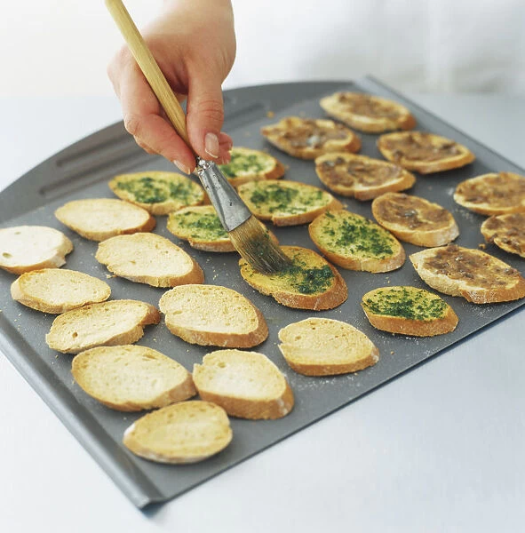 Using a brush to spread toppings on slices of bread on a tray