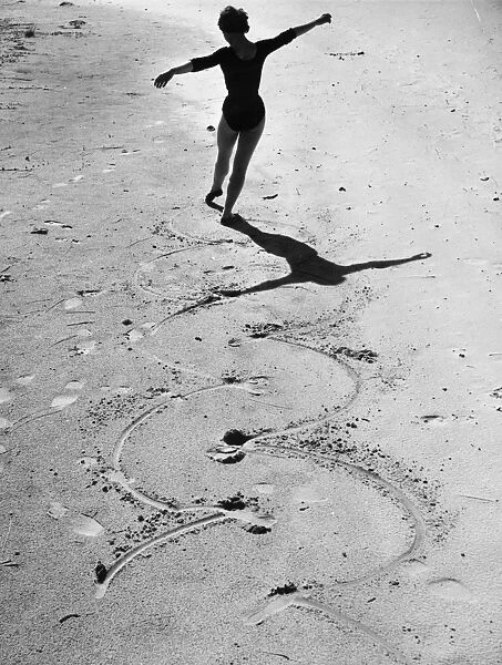 Beach Ballet. August 1955: A ballet dancer draws circles in the sand with