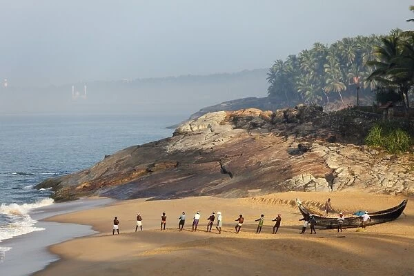 Fishermen pulling in a net, beach south of Kovalam, Vizhinjam in the distance, Malabar Coast, Malabar, Kerala, southern India, India, Asia