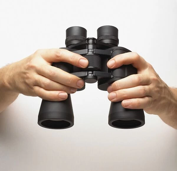 Hands holding binoculars, finger turning central knob, adjusting focus