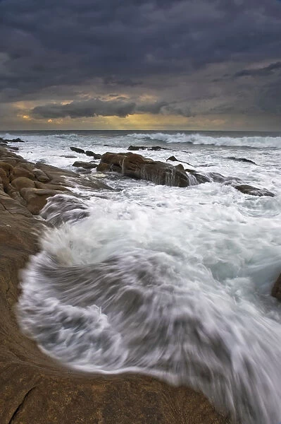 Landscape photo of ocean waves crashing onto the rocks under a stormy moody sky at sunrise. Durban, Kwazulu-Natal, South Africa