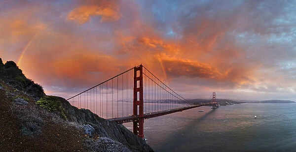 Panoramic view of the Golden Gate Bridge with a rainbow at sunset and orange-glowing storm clouds, San Francisco, California, United States