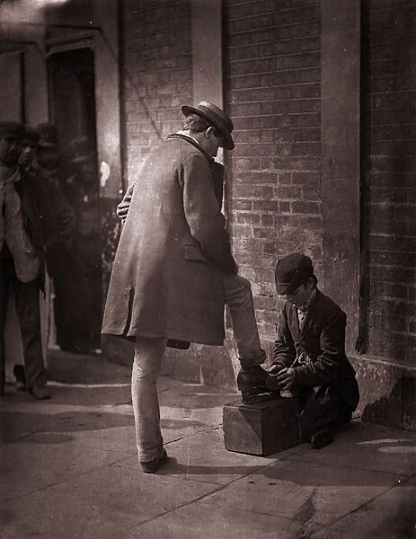 Shoeshine. 1877: A young independent shoeblack shines the boots of a city gent