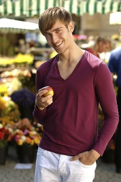 Young happy man holding an apple at a market