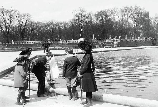 Jardin du Luxembourg - France, Ile-de-France, Paris (75): children disguises as sailor and gendarme at the edge of the basin put a sailboat (toy) in the water, 1895